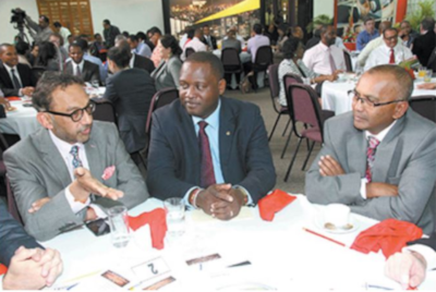 The Honorable Donville O. Inniss, Minister to the Ministry of Industry, International Business, Commerce and Small Business Development meeting with a few gentleman at a dining table. Many other people seated behind them at other tables.