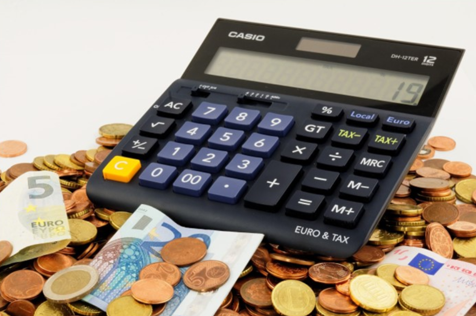 A large calculator sitting atop a pile of euros, both paper and coins.