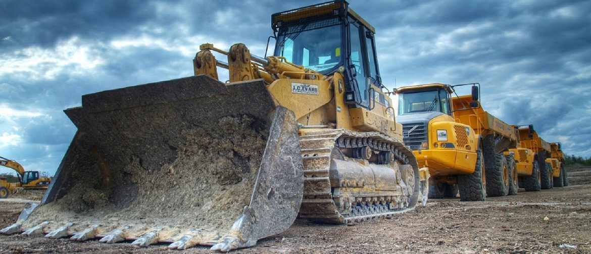 Lydford Mining. A bulldozer with a bucket on front follow by other work vehicles. Overcast sky with light showing through.