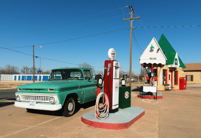 A classic truck pulled up to an old time, glass dome, gasoline pump.