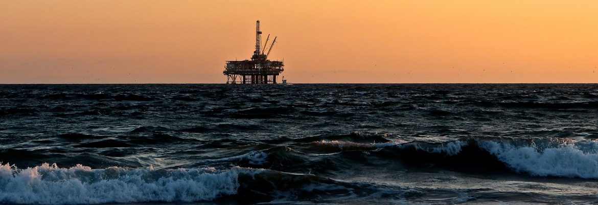 An oil rig off the coast in the middle of the ocean near sunset.