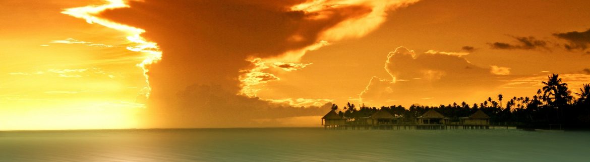 Ocean view with an island on the right and orange sky with clouds and the sun on the horizon.