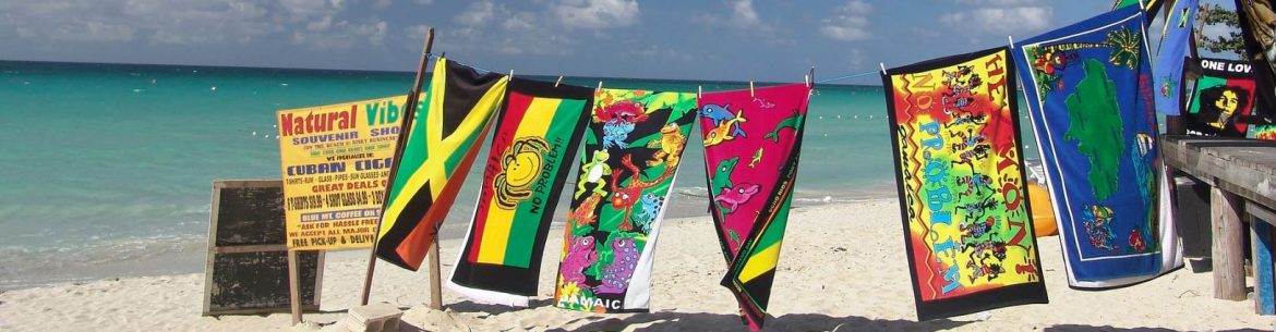 A clothing line along a caribbean beach, with beach towels pinned to it outside of a shop to the right.