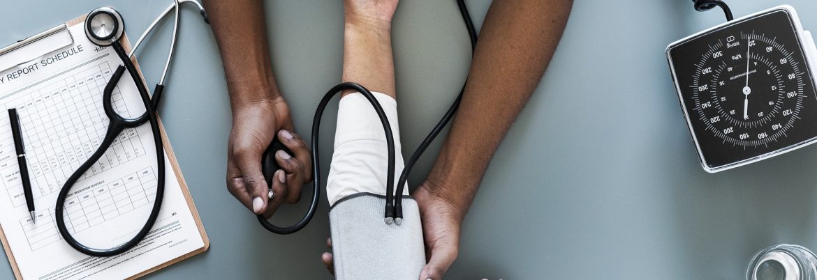 Caribbean Heart Care Medcorp. Arms from someone administering a blood pressure test with a clipboard and stethoscope on the table.