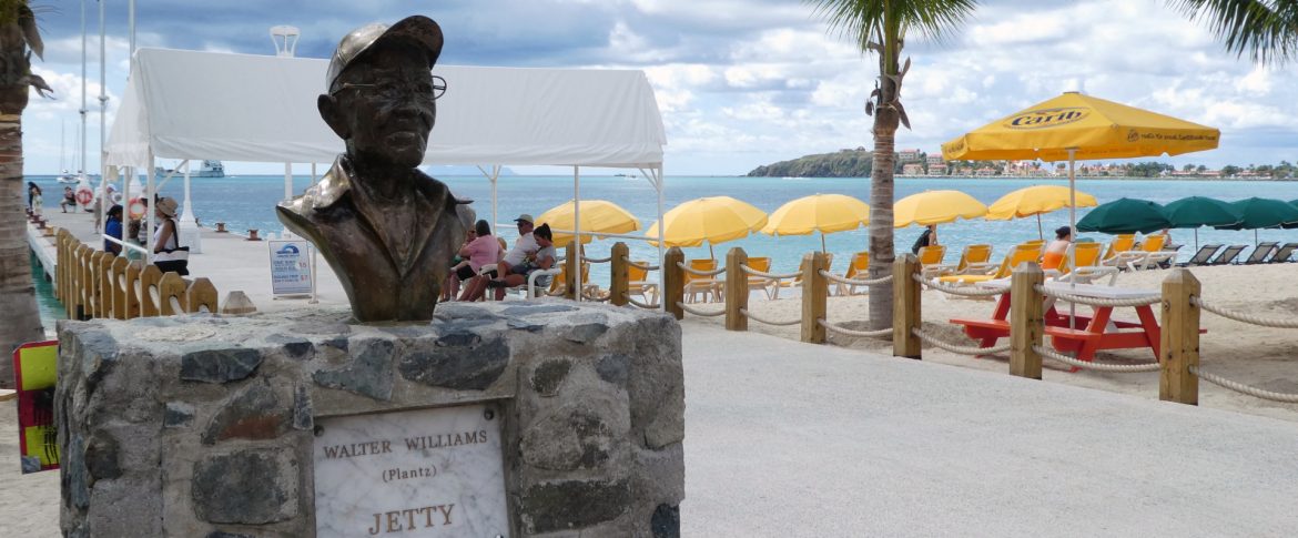 Port St. Maarten Group of Companies; View of a jetty on a beach with umbrellas and ocean behind.