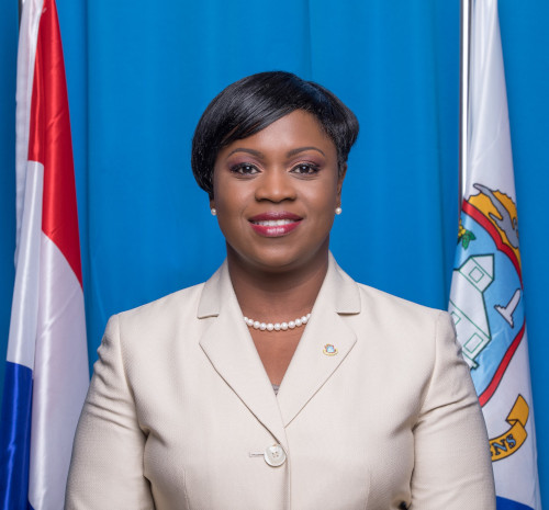 Prime Minister of St. Maarten, Leona Romeo-Marlin standing with two flags behind her.