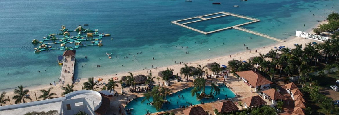 Puerto Seco Beach aerial view showing the dolphin area and a floating obstacle course on the water along the beach.