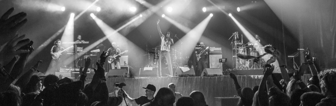 Black and white photo of a band on stage with fans in front and stage lights behind shining. Jamaica’s ‘Voices for Climate Change’ Spreads its Message with Music