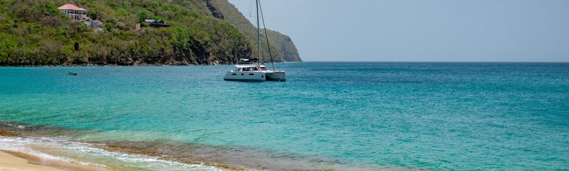St. Vincent and the Grenadines ocean view with a catmaran sailboat in the water and a few buildings on the green mountainside behind.