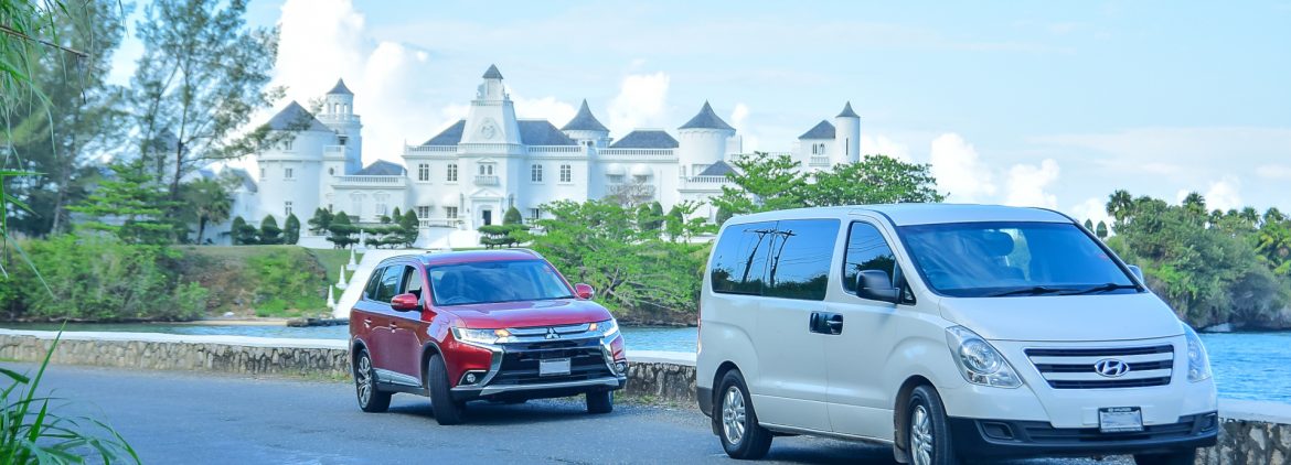 Island Car Rentals Jamaica two vehicles on the road in front of a nice large estate.