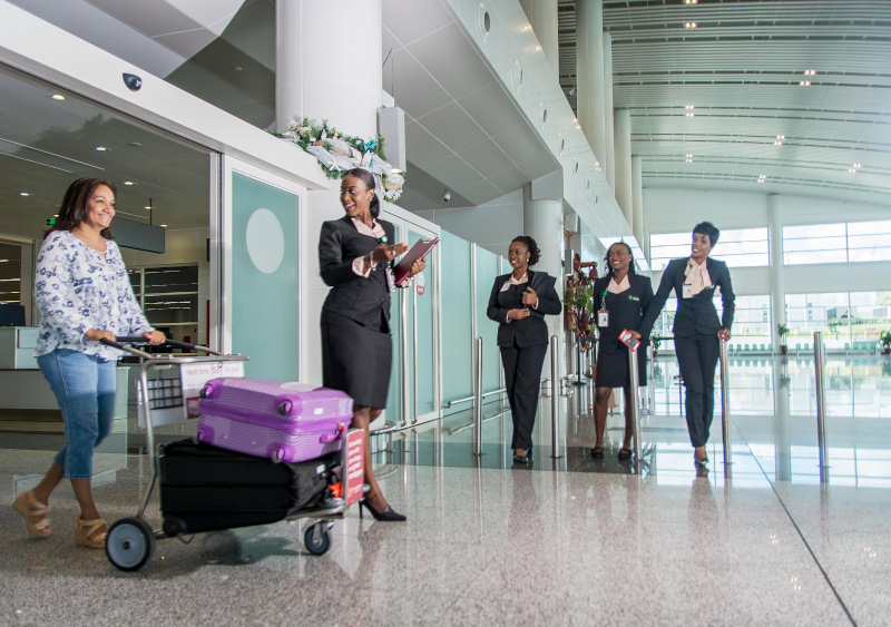 VC Bird International Airport manage by Antigua and Barbuda Airport Authority. Female employees greeting a woman traveler pushing luggage.
