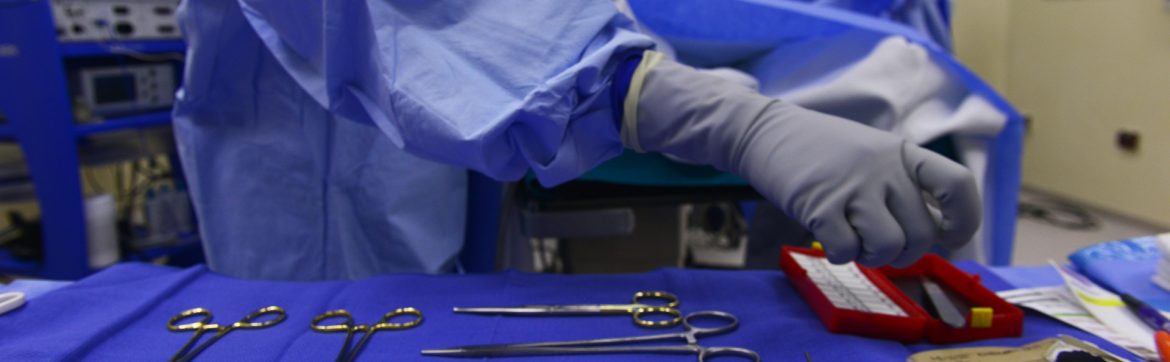 Falmouth Public General Hospital, stock image showing someone in scrubs and gloves reaching for tools during a medical procedure.