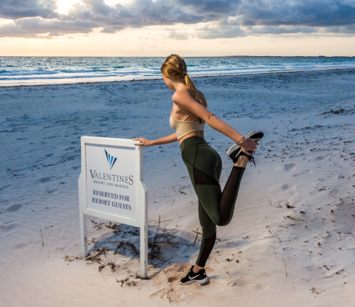 Valentines Residences, Resort & Marina Bahamas showing a woman stretching while leaning on a sign on the beach.