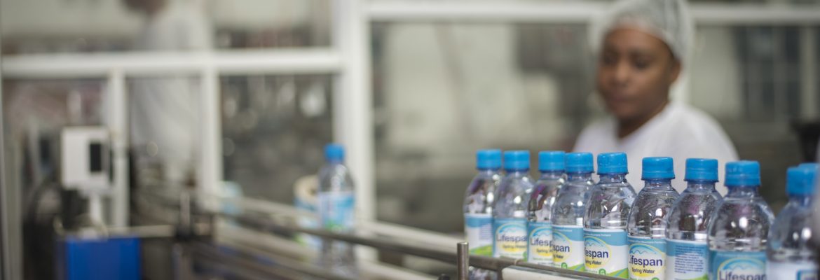 Lifespan Company Ltd employee with hairnet overlooking bottling line for water.