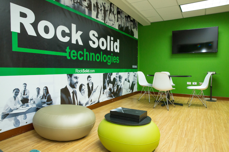 Rock Solid Technologies Puerto Rico office interior showing their sign on the wall and table and chairs with a tv on the wall.