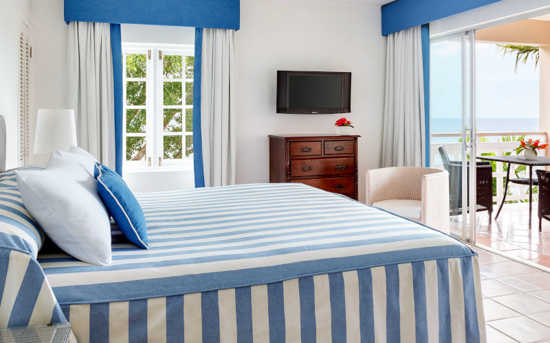 Couples San Souci Jamaica, a vibrant white and blue bedroom interior with a beach view visible in the corner beyond the patio.