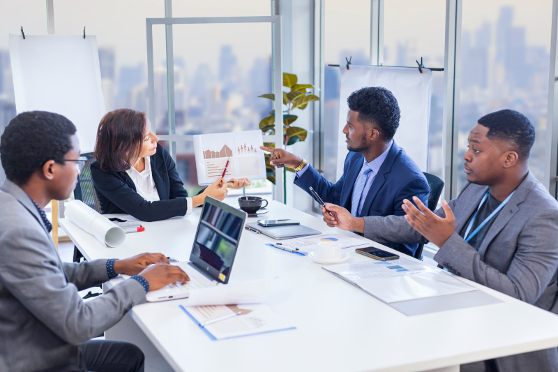 Woman manager is showing annual report chart to her African American colleagues in the executive meeting for next year plan with city skyline background for global business and investment